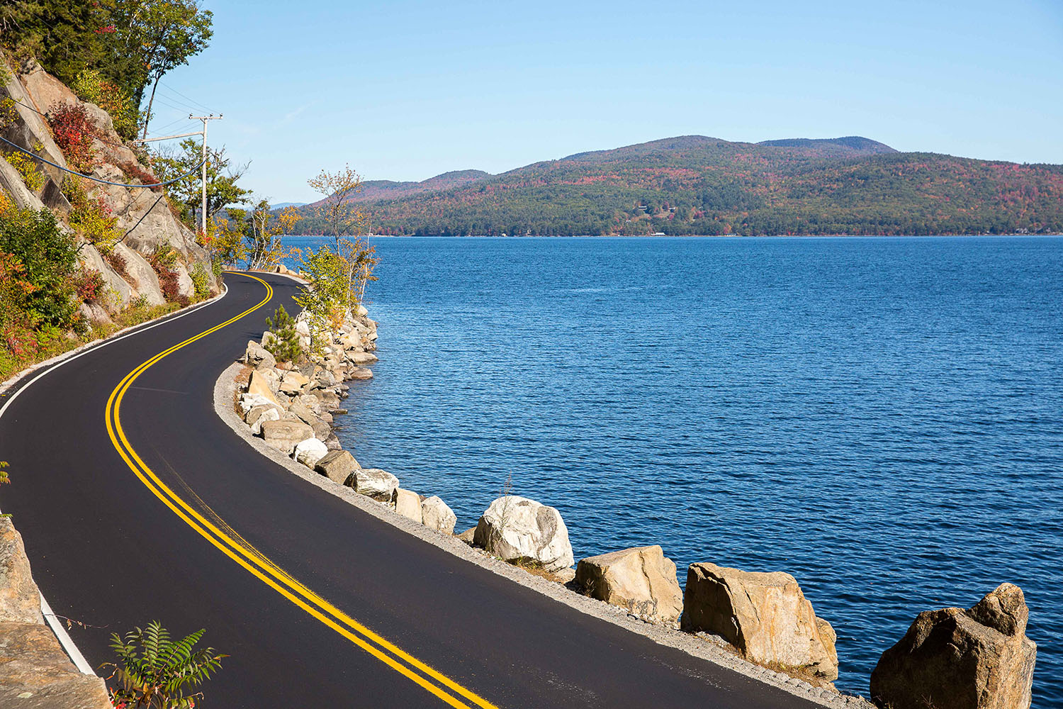 a road next to a lake surrounded by fall foliage