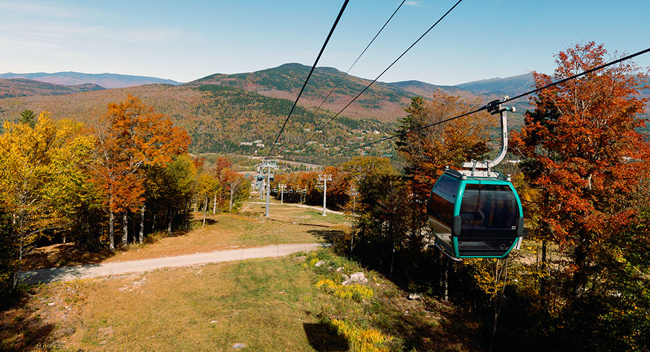 a gondola climbing a mountain with fall foliage surrounding