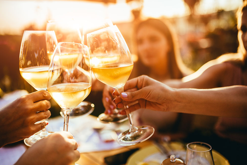 four glasses of wine being clinked over a table in sunshine