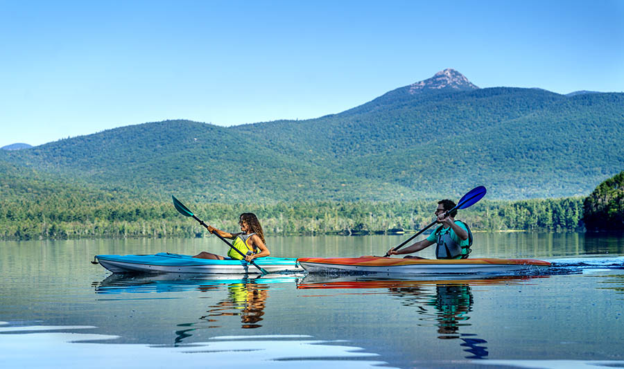 a man and woman kayaking in a lake with a mountain behind them