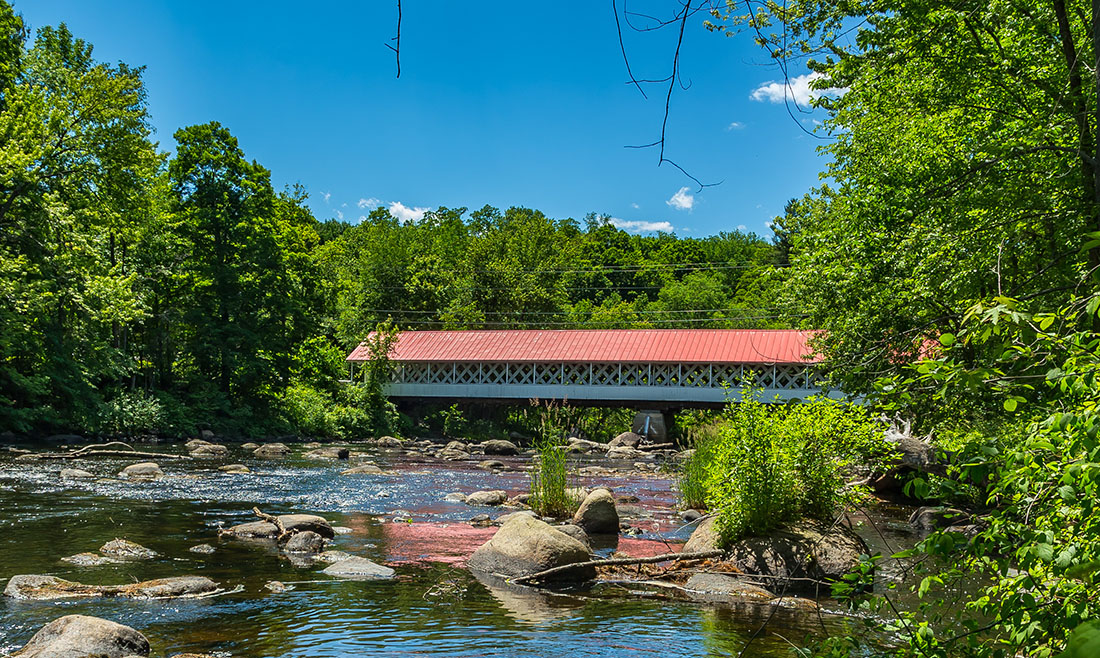 a covered bridge with a red roof over a river surrounded by green trees.