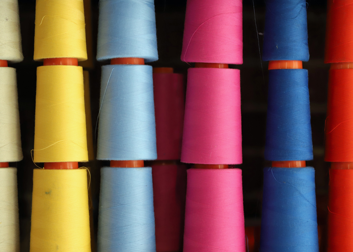 Yellow, light blue, pink and dark blue spools of thread.
