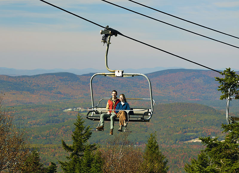 a man and woman riding on a chairlift in fall