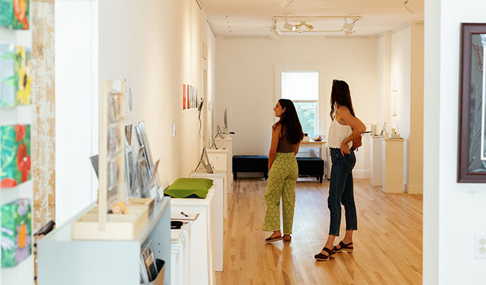 Two women inside an art gallery looking at art on the wall.