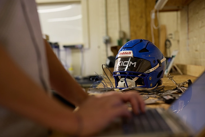A shot of someone working on a laptop with a helmet in the background
