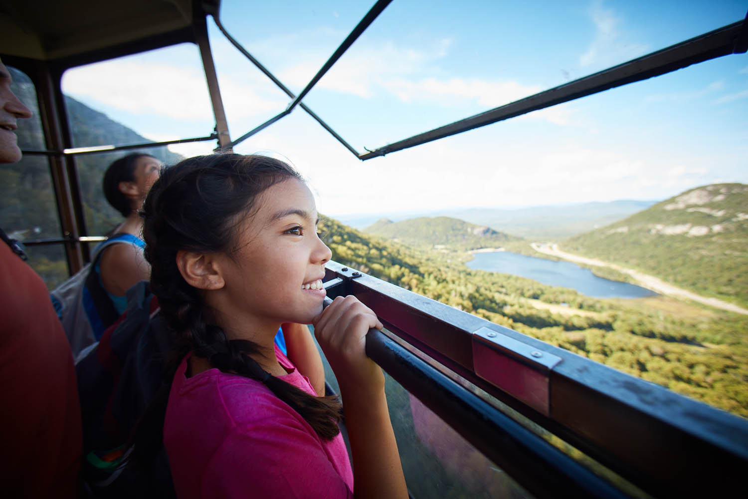a little girl looking out the window of an aerial tram with a large lake in the view.