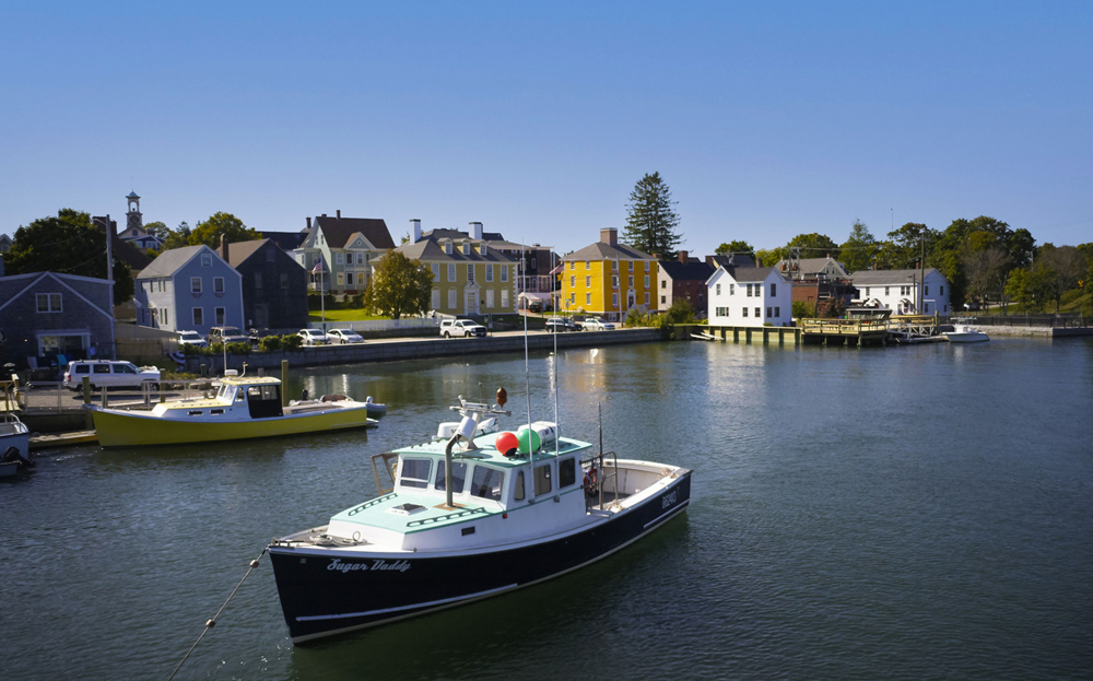 a boat off the coast with a shoreline full of quaint colorful houses.