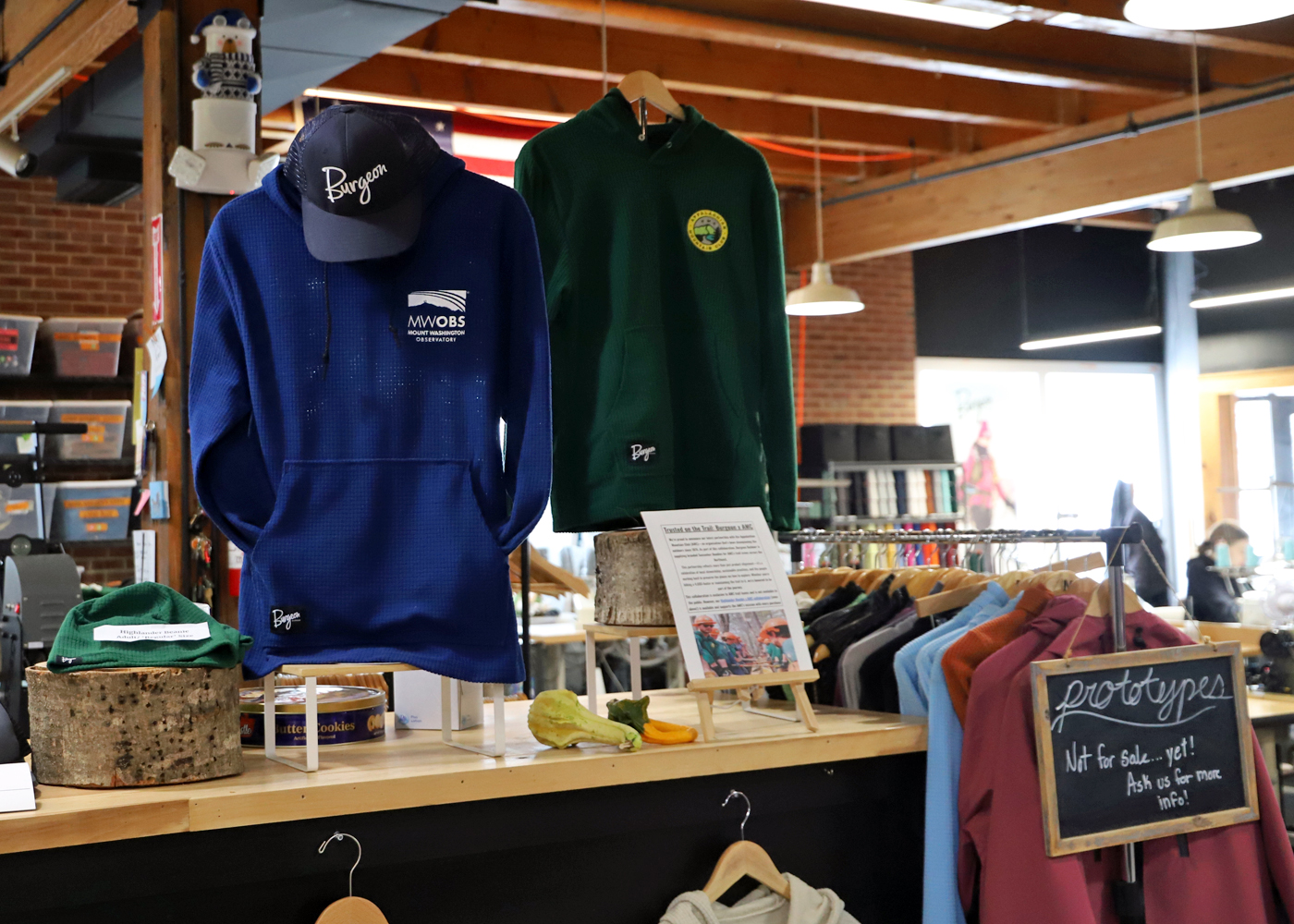 Store with jackets hanging and a hat, with clothing rack in background