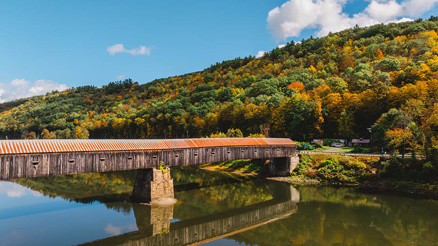 a view of a wooden covered bridge with fall foliage in the background.