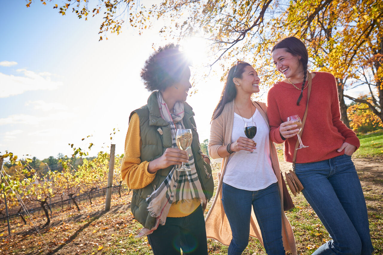 three woman drinking wine outside at a vineyard in fall