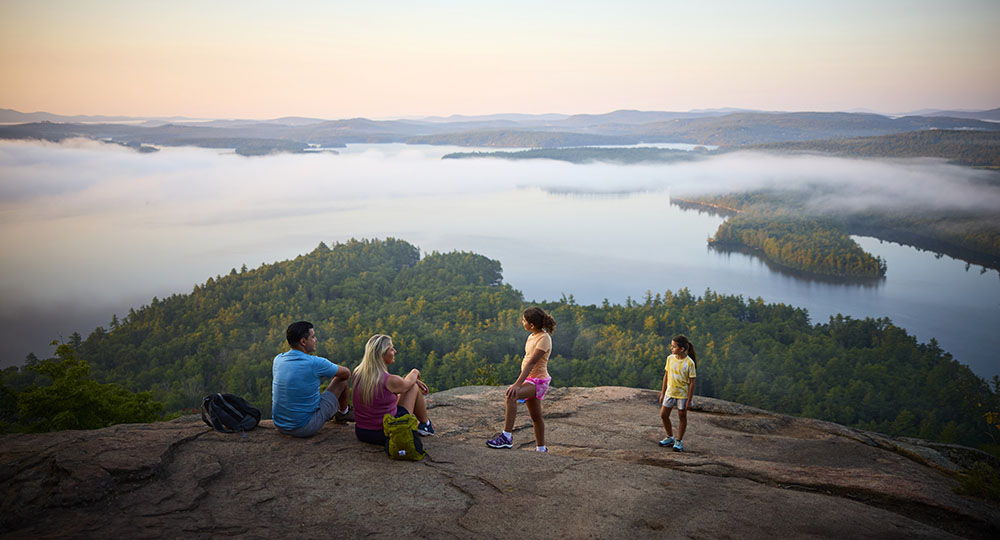 a family sitting on a rocky mountaintop overlooking a lake below