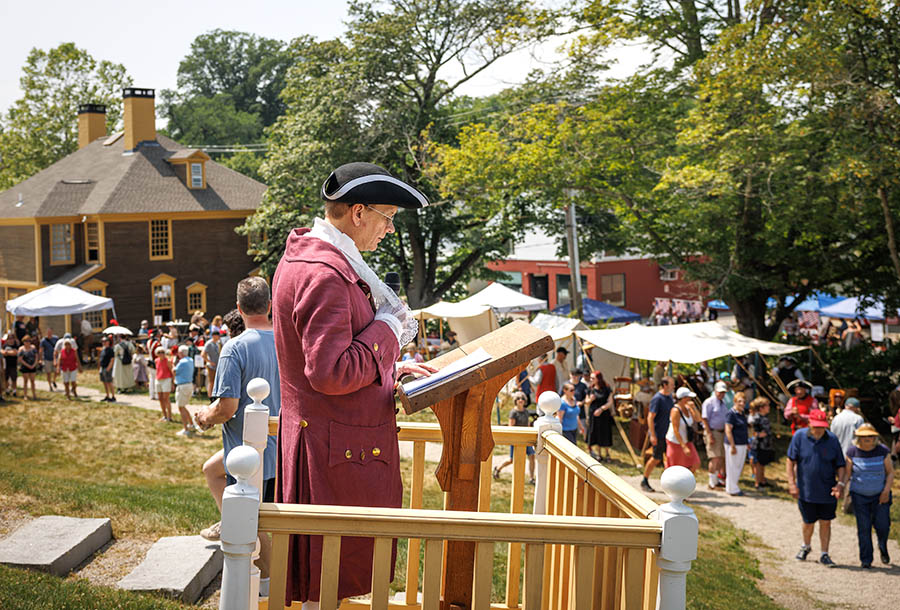 a man in historical dress giving a speech at a podium at an outdoor event