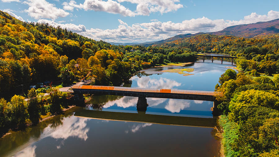 a long covered bridge spanning a river, surrounded by fall foliage