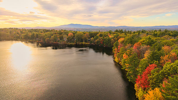 a view of a lake in fall with foliage surrounding the shores and a mountain in the background.