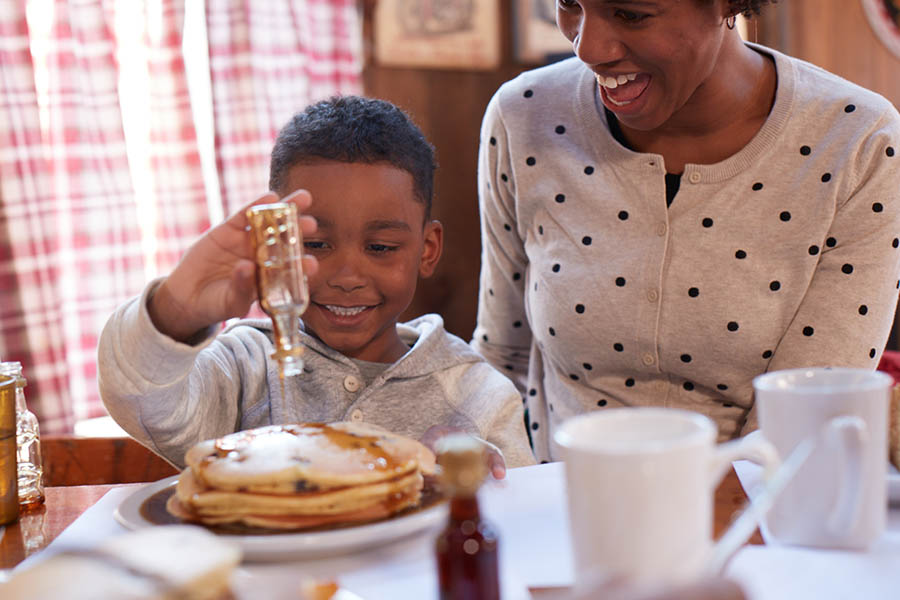 a boy pouring maple syrup onto a pile of pancakes