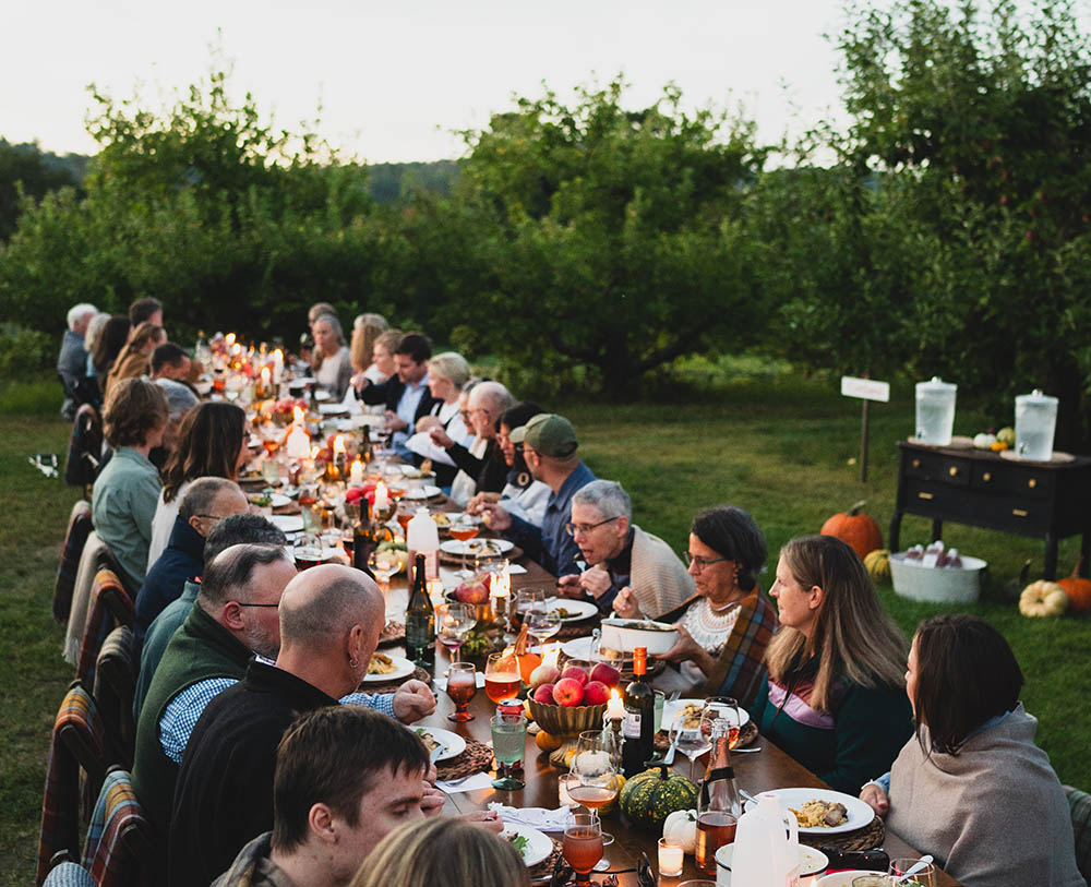 a group of people dining outdoors at a table set with fall decor in an orchard