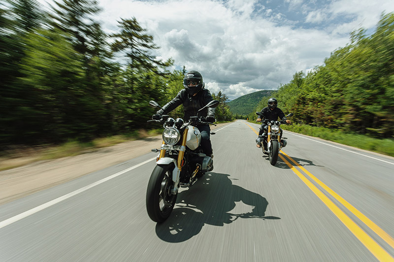 two motorcycles on a road surrounded by green trees.