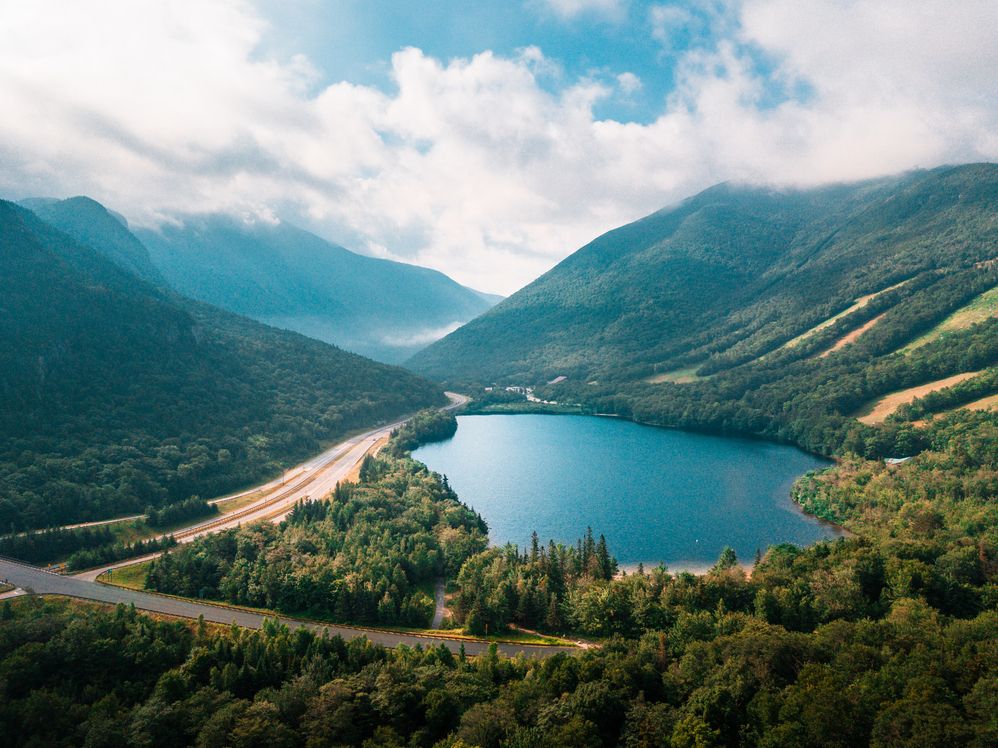 A view of a lake with a road next to it and mountainside with ski trails in summertime.