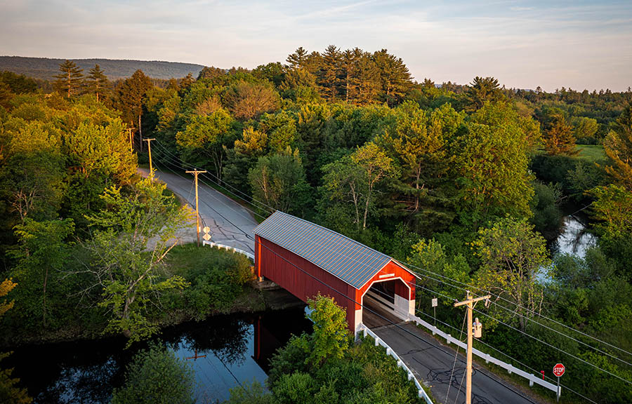 aerial view of a red covered bridge with trees surrounding.