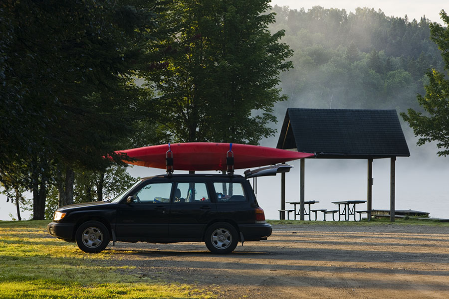 a car with a kayak on the roof by a lake