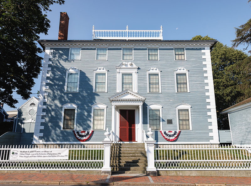 a grey historic building with flags and a fence out front