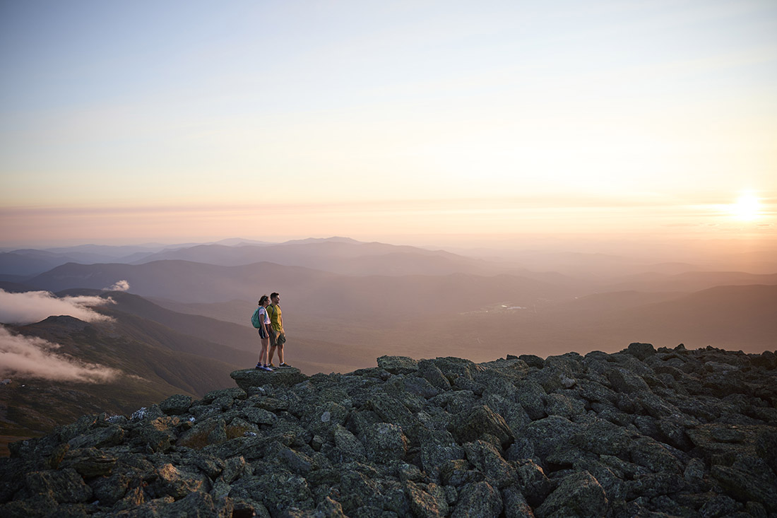 two hikers on a rock at sunset