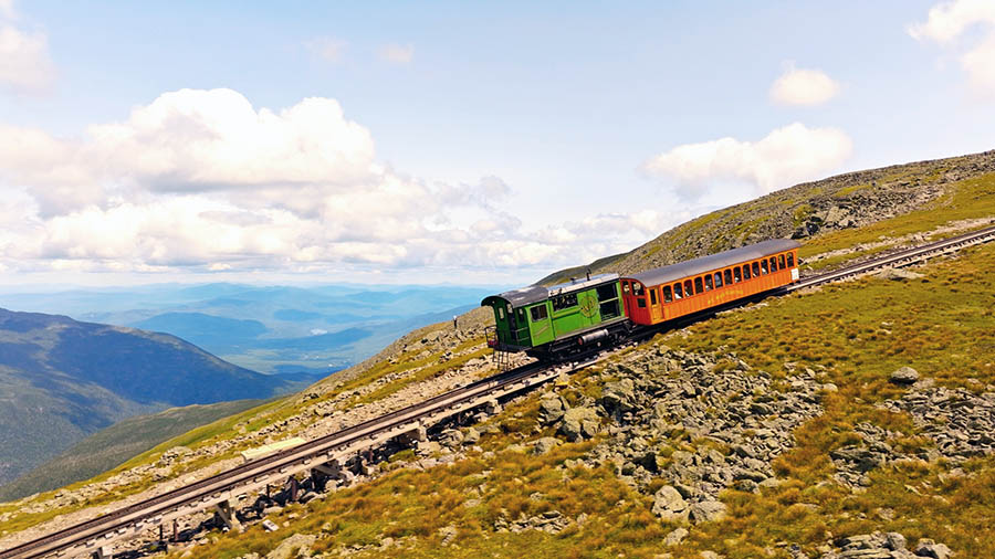 A train climbing a rocky mountain with many mountains in the background.