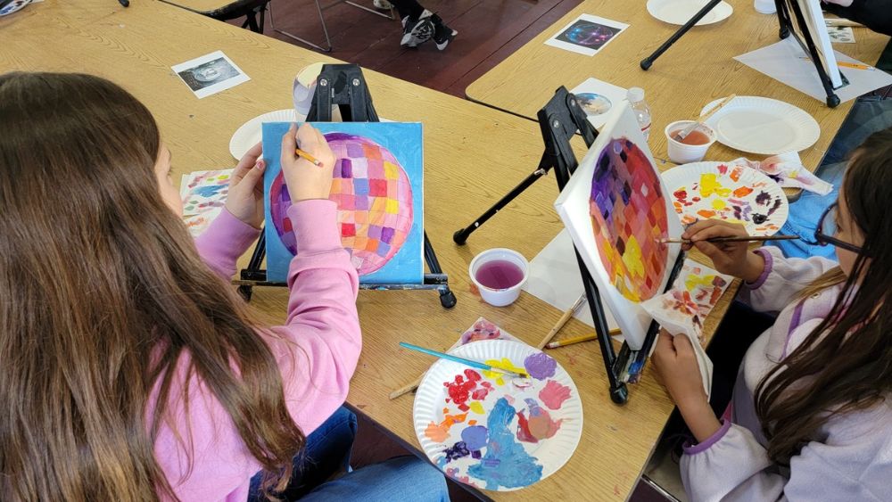 Image decpiting two kids painting during an art class