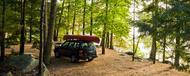 A car with a canoe on the roof parked in a wooded campsite