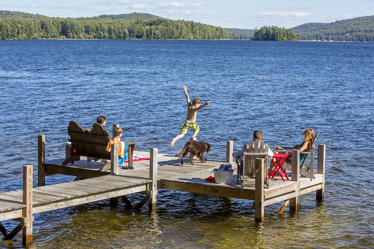 family sitting on dock and child jumping in the water
