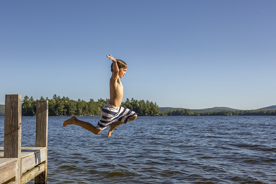 a young boy jumping off a dock into a lake