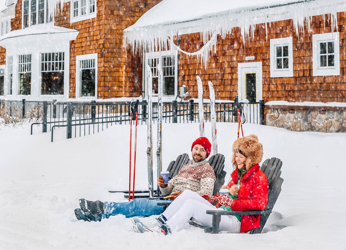couple outside in the snow with hot cocoa sitting on chairs