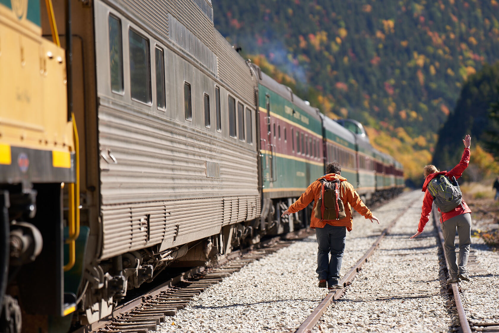 a man and woman walking next to a train in the mountains