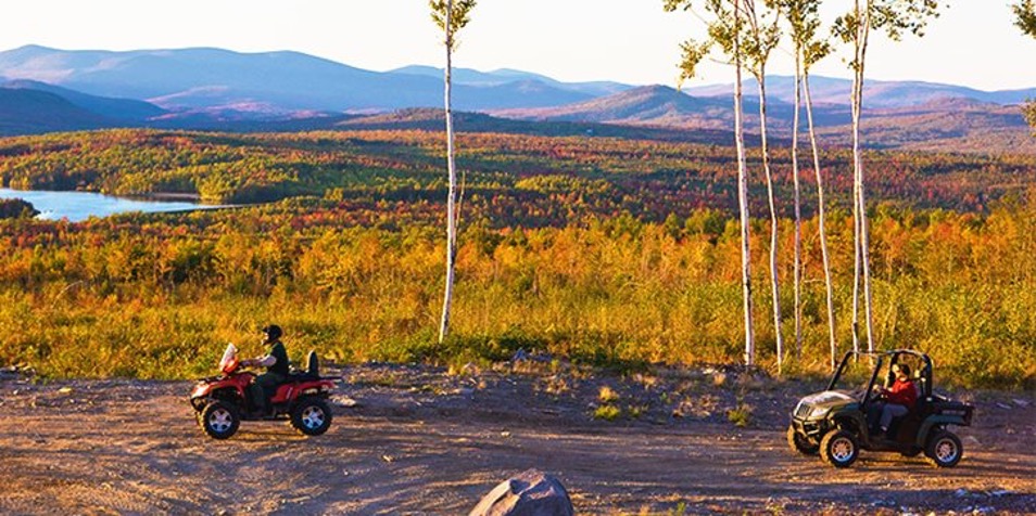 Someone driving an ATV in front of mountains of fall foliage